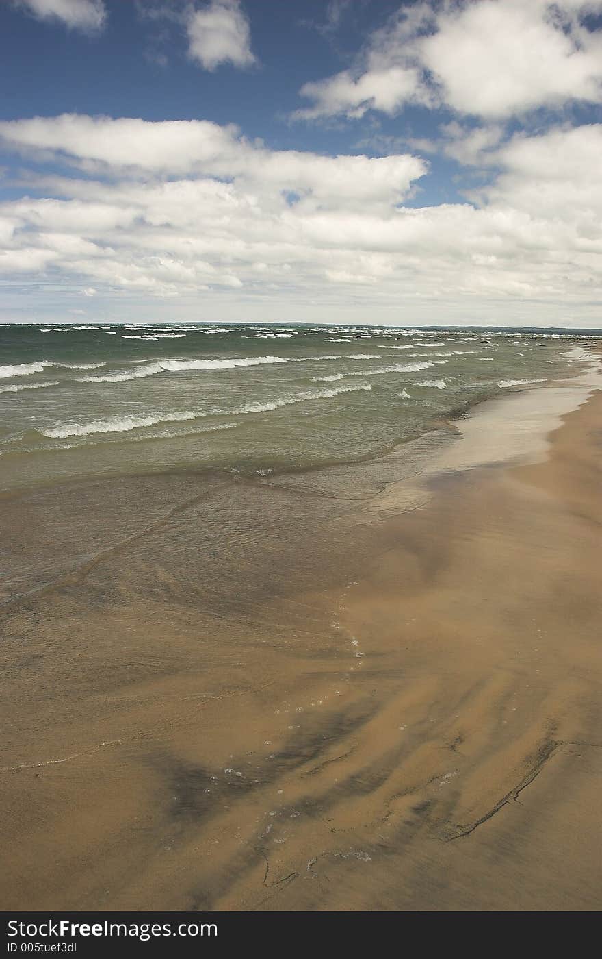 Waves crash along an empty beach on a sunny summer day. Waves crash along an empty beach on a sunny summer day