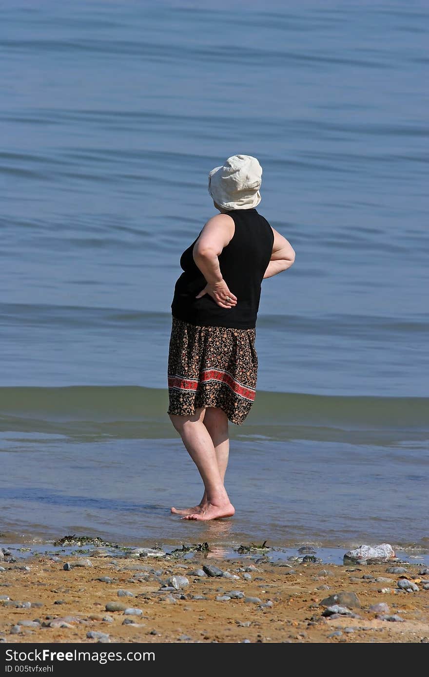 Elderly female at the beach, barefoot and paddling in the sea. Elderly female at the beach, barefoot and paddling in the sea.