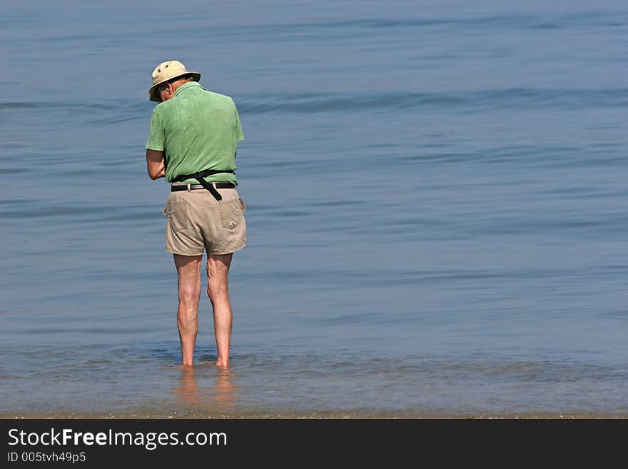 Elderly man paddling at the beach and looking at something in the water. Elderly man paddling at the beach and looking at something in the water.