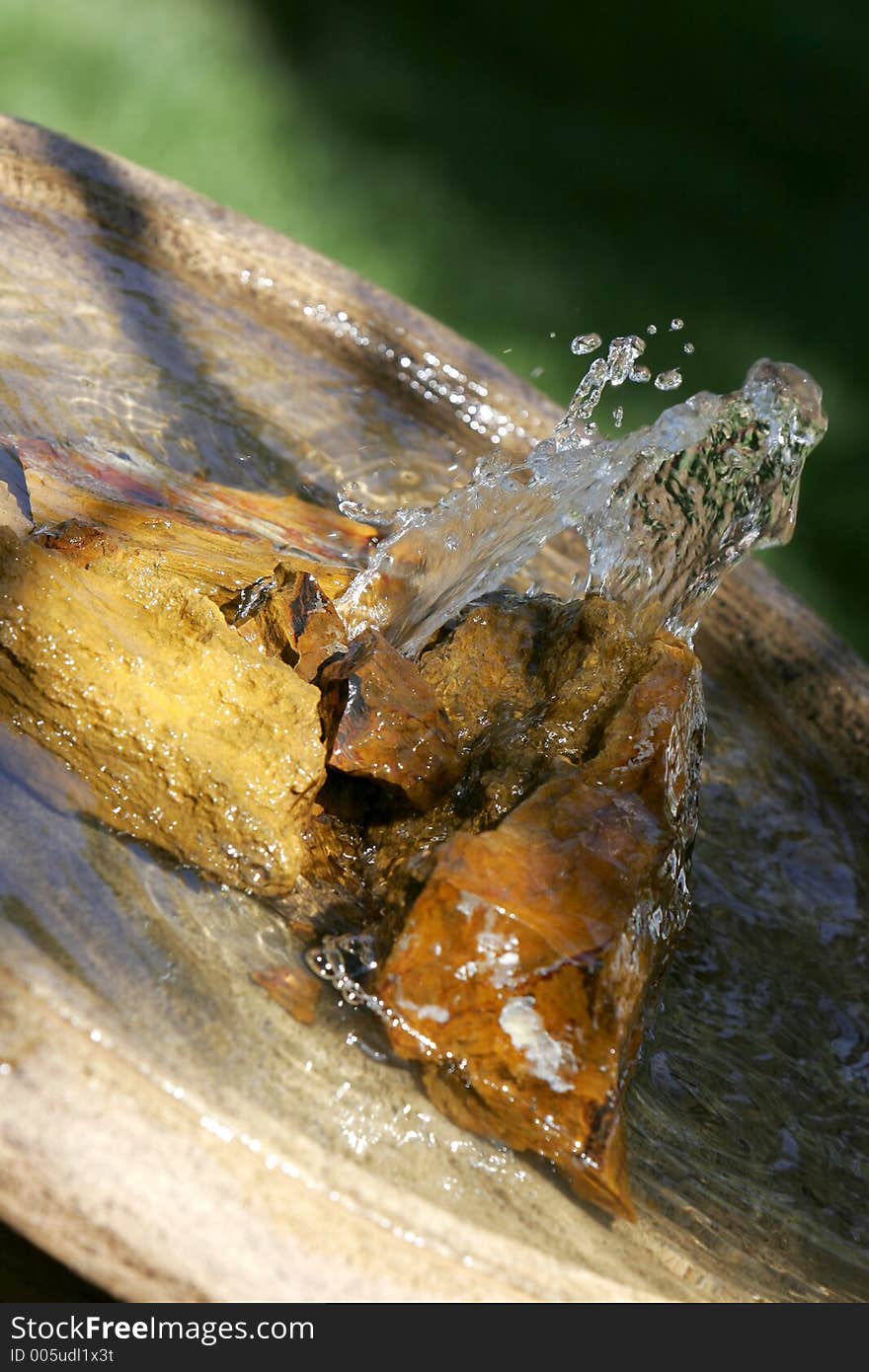 Angled close-up of a peaceful fountain in sunlight and shade, with petrified wood and pool of water (shallow focus). Angled close-up of a peaceful fountain in sunlight and shade, with petrified wood and pool of water (shallow focus).