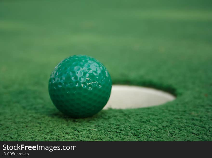 A miniature golf ball near the hole. A miniature golf ball near the hole