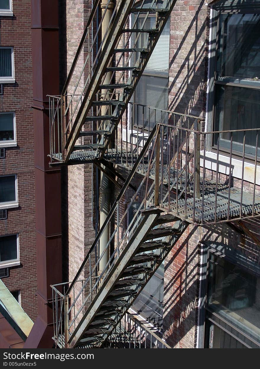 Old fire escape on apartment building, in bright sunshine showing two levels and part of the back of the brick building. Old fire escape on apartment building, in bright sunshine showing two levels and part of the back of the brick building