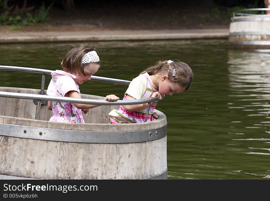 Twins playing on a playground, making a boat trip on the water in a barrel. Twins playing on a playground, making a boat trip on the water in a barrel