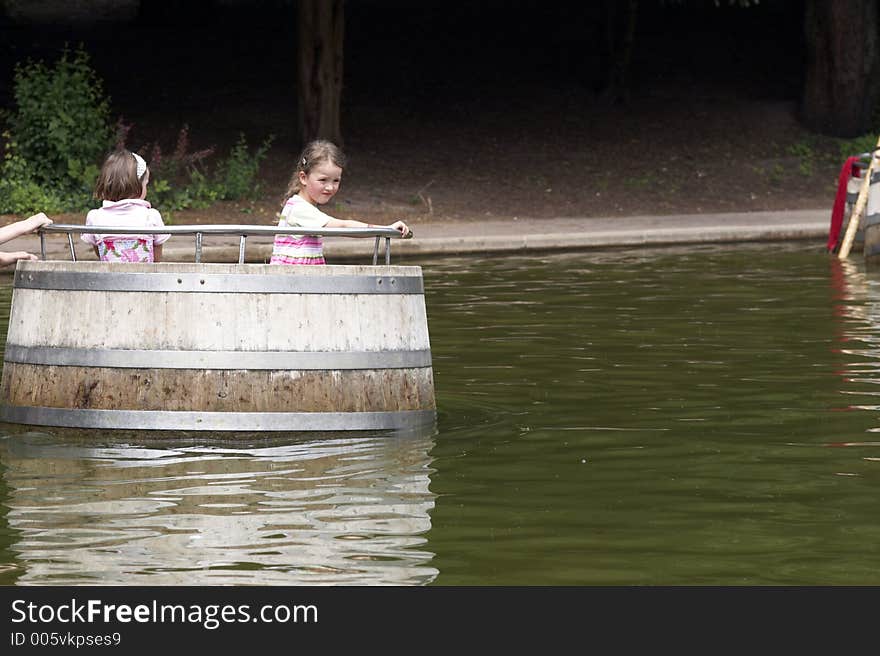 Twins playing on a playground, making a boat trip on the water in a barrel. Twins playing on a playground, making a boat trip on the water in a barrel