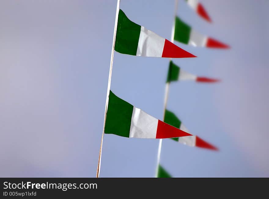 Some small Italian flags on a blue sky background, short depth of field, first row in focus and second row blurred