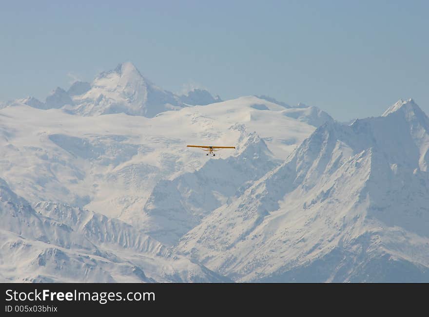 A yellow plane equipped with skis flying in the Swiss mountains. A yellow plane equipped with skis flying in the Swiss mountains.