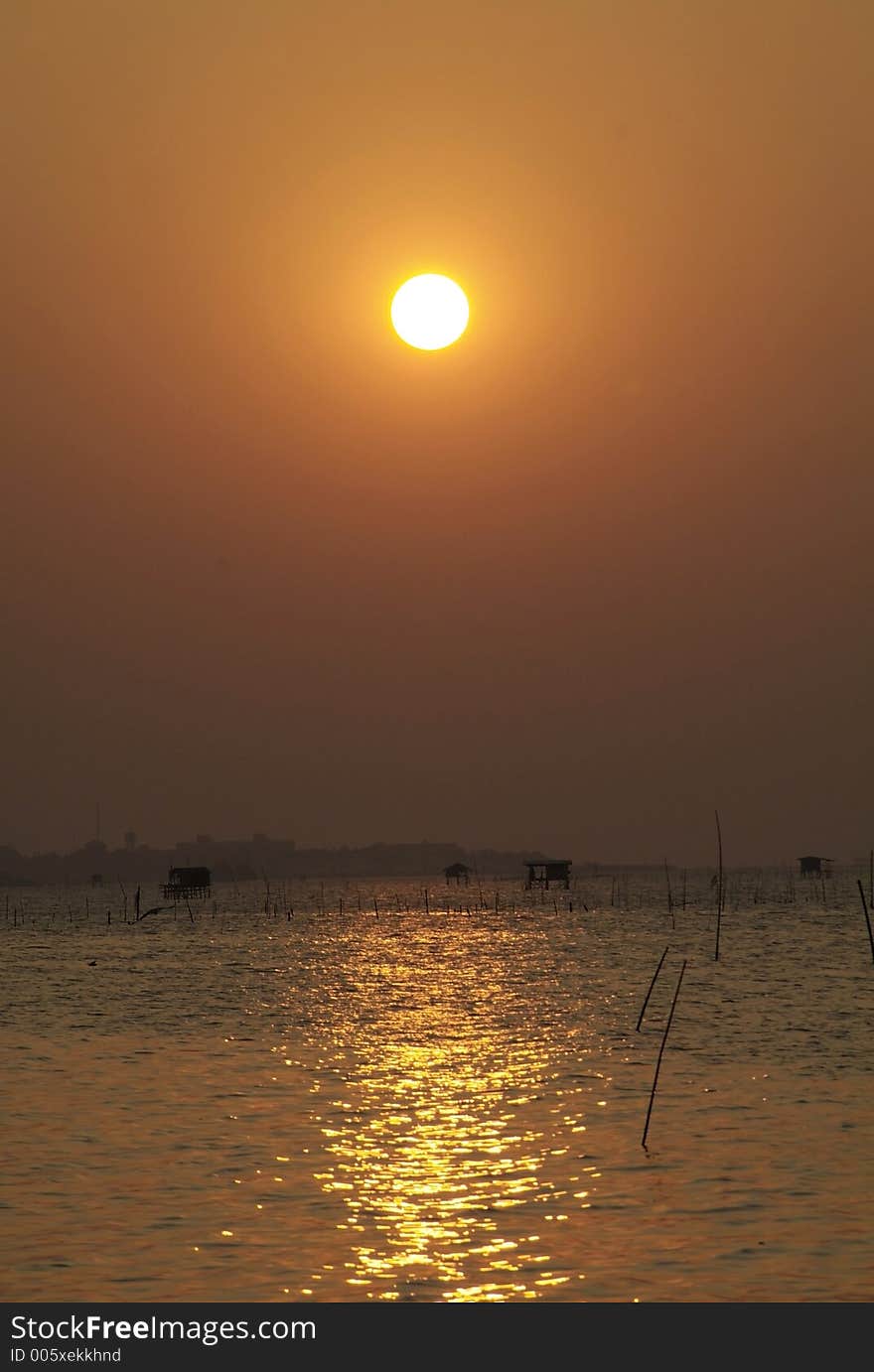 Golden sunset over Gulf of Siam seen from at Chonburi on Thailand's eastern seaboard. Fisherman's huts on stilts in the shallow water. Golden sunset over Gulf of Siam seen from at Chonburi on Thailand's eastern seaboard. Fisherman's huts on stilts in the shallow water.