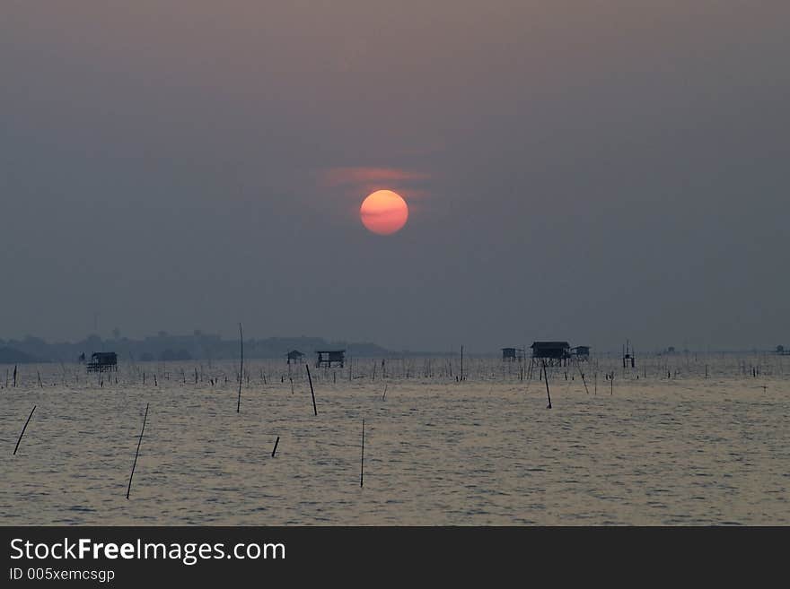 Cloudy sunset at Chonburi on Thailand's eastern seaboard with fishermens huts standing in the shallow waters. Cloudy sunset at Chonburi on Thailand's eastern seaboard with fishermens huts standing in the shallow waters