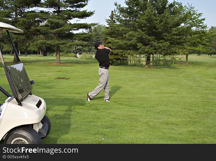 Man driving a ball from the fairway, golf cart in foreground.