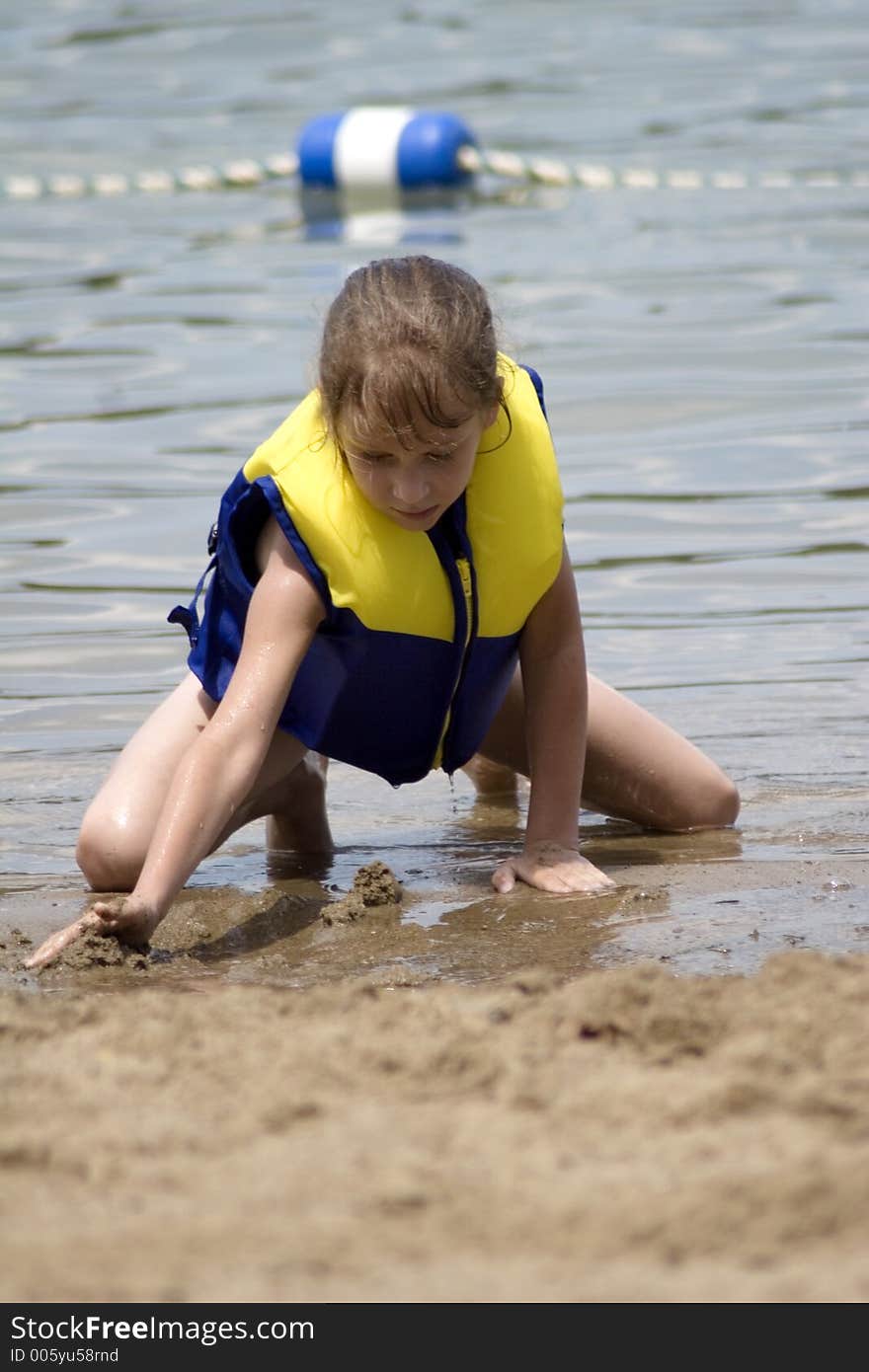 Young girl in lifejacket playing in the beach sand at the lake. Young girl in lifejacket playing in the beach sand at the lake.