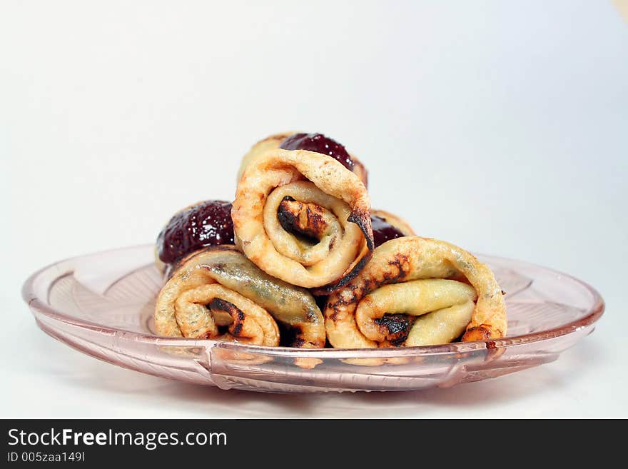 Rolled pancakes with sweet strawberry jam on a transparent glass plate. Rolled pancakes with sweet strawberry jam on a transparent glass plate