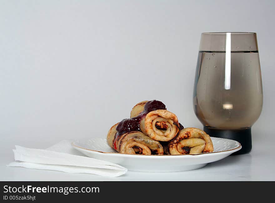 Rolled pancakes with sweet strawberry jam and glass of fresh mineral cool water. Rolled pancakes with sweet strawberry jam and glass of fresh mineral cool water