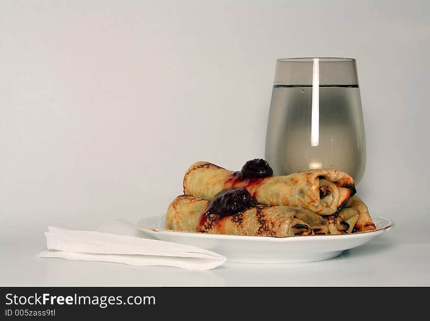 Rolled pancakes with sweet strawberry jam and glass of fresh mineral cool water. Rolled pancakes with sweet strawberry jam and glass of fresh mineral cool water