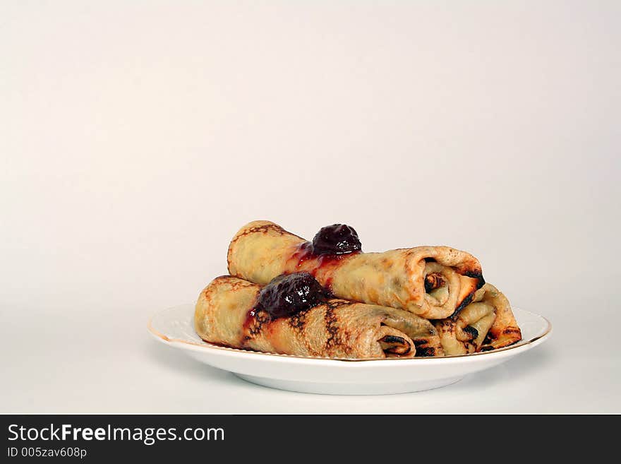 Rolled pancakes with sweet strawberry jam on a white ceramic plate. Rolled pancakes with sweet strawberry jam on a white ceramic plate