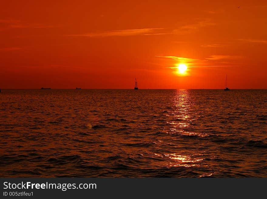 Beautiful sunset with clear orange sky and sailboats in the background