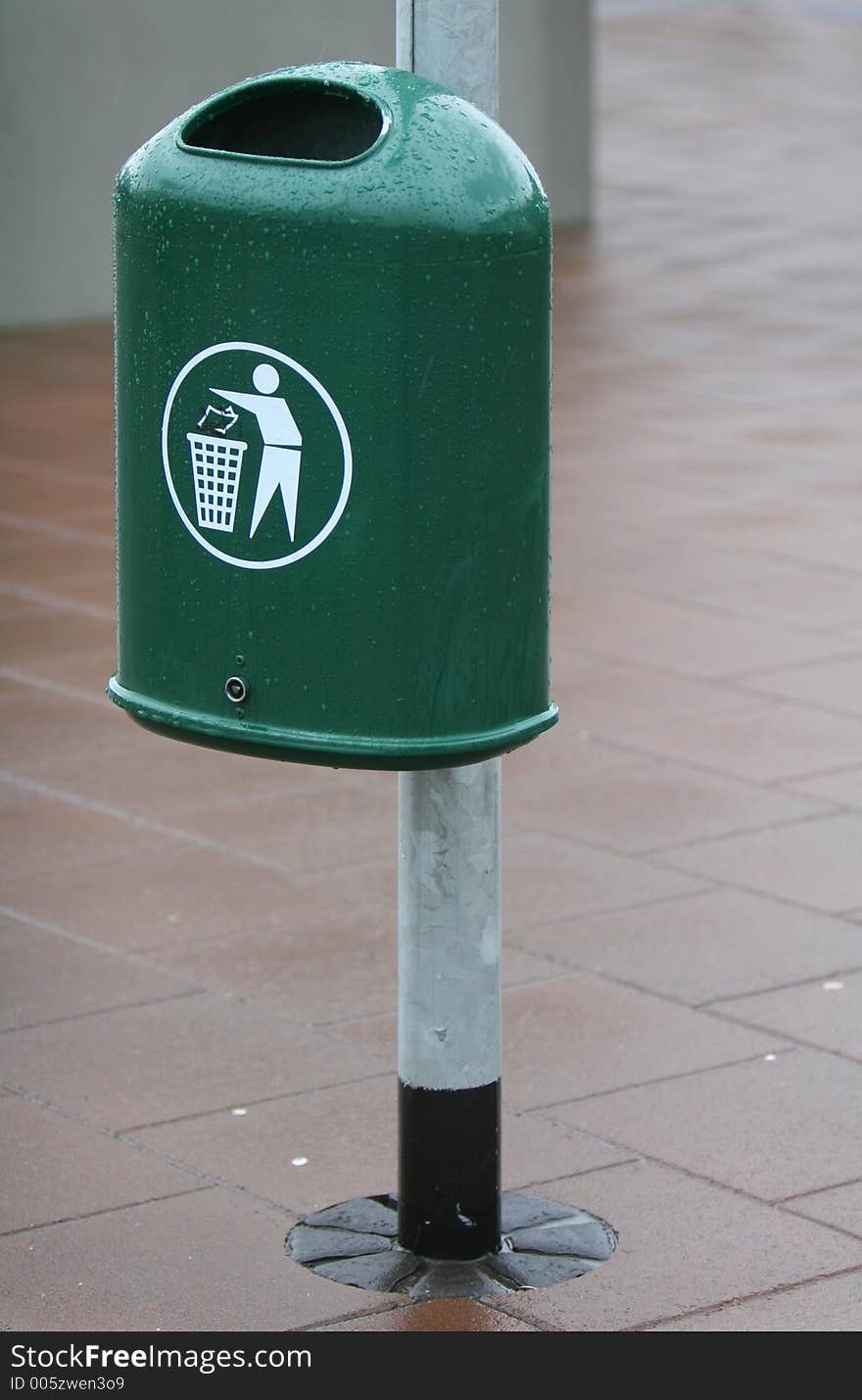 A green trash bin in a city. The Bin is fastened to a lightpole. A green trash bin in a city. The Bin is fastened to a lightpole.