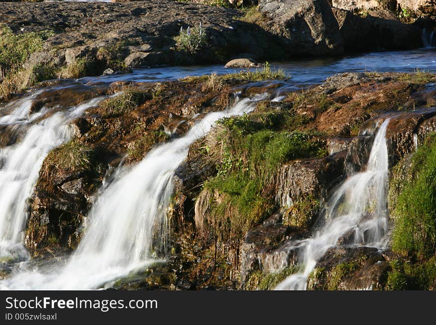 Photograph of small river, flowing, waterfalls, lush green vegetation and genuine tranquil athmosphere