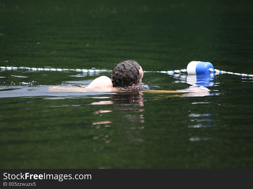 A man swims inside a roped area of a resort lake beach. A man swims inside a roped area of a resort lake beach