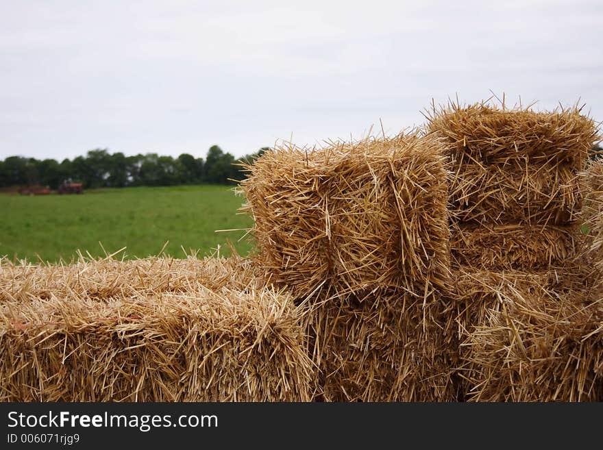 A wagon of straw in the foreground with a farmer working in the background. A wagon of straw in the foreground with a farmer working in the background