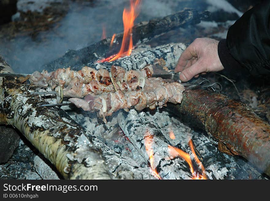 Grilled pork on bonfire and man hand