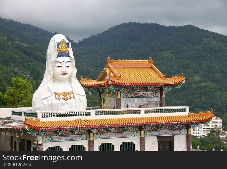 Large statue of a Buddha and an elaborate Chinese style temple in front of tree covered mountain. Large statue of a Buddha and an elaborate Chinese style temple in front of tree covered mountain