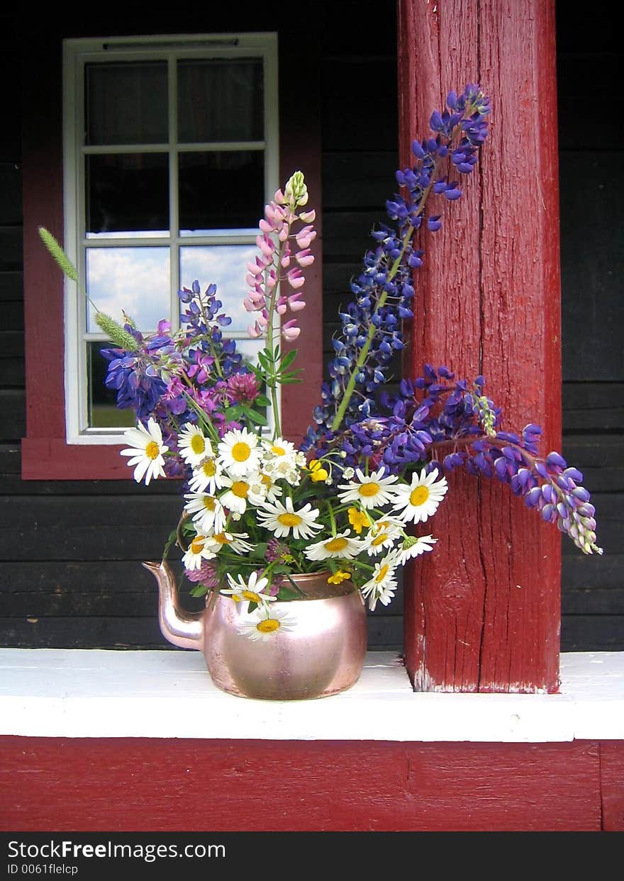 Copper coffee pot with wild flowers standing on a porch. Copper coffee pot with wild flowers standing on a porch