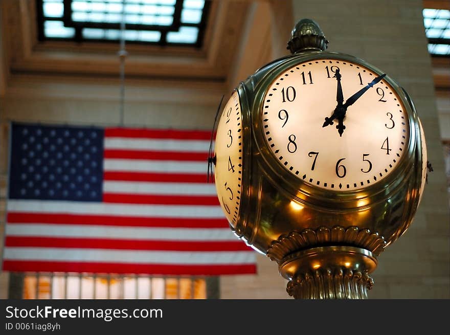 Clock on Information Booth at Grand Central Station New York City. The American flag is blurred in the background. The time is just past high noon. Clock on Information Booth at Grand Central Station New York City. The American flag is blurred in the background. The time is just past high noon