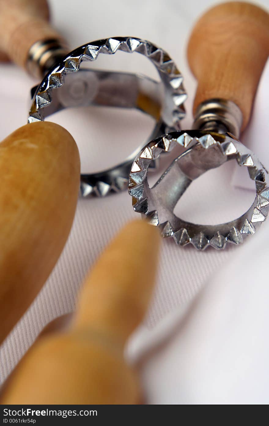 Macro, shallow depth of field view of ravioli, pasta or pastry cutters and rolling pins. Background is the white linen of a chef uniform. Macro, shallow depth of field view of ravioli, pasta or pastry cutters and rolling pins. Background is the white linen of a chef uniform.