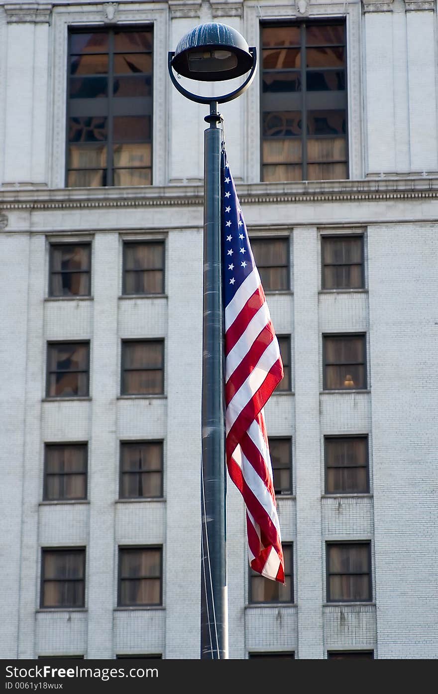 The flag of the United States hangs from a pole with an older building as the background. The flag of the United States hangs from a pole with an older building as the background