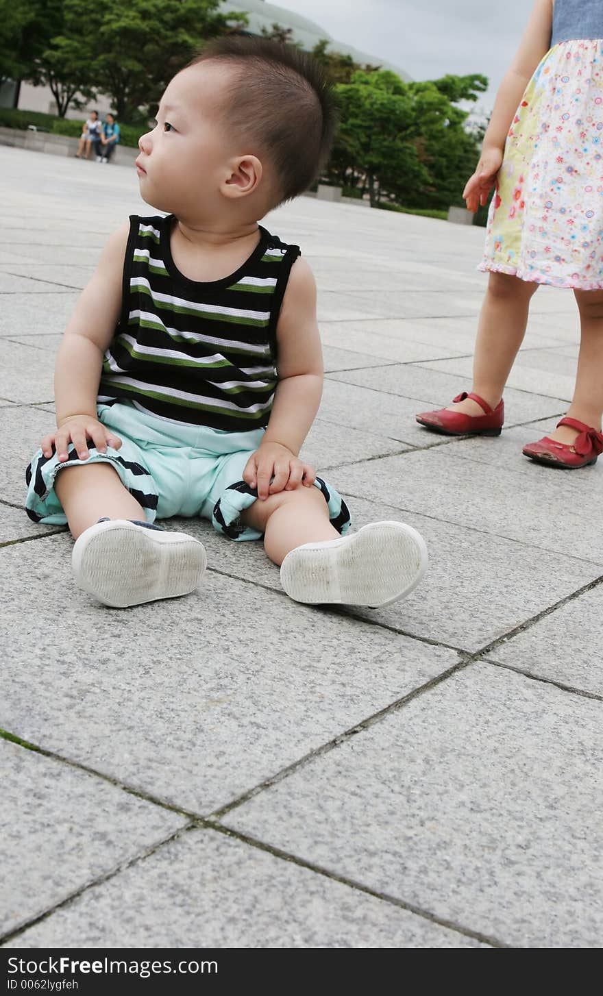 Cute Asian boy sitting on the ground - girl in the background