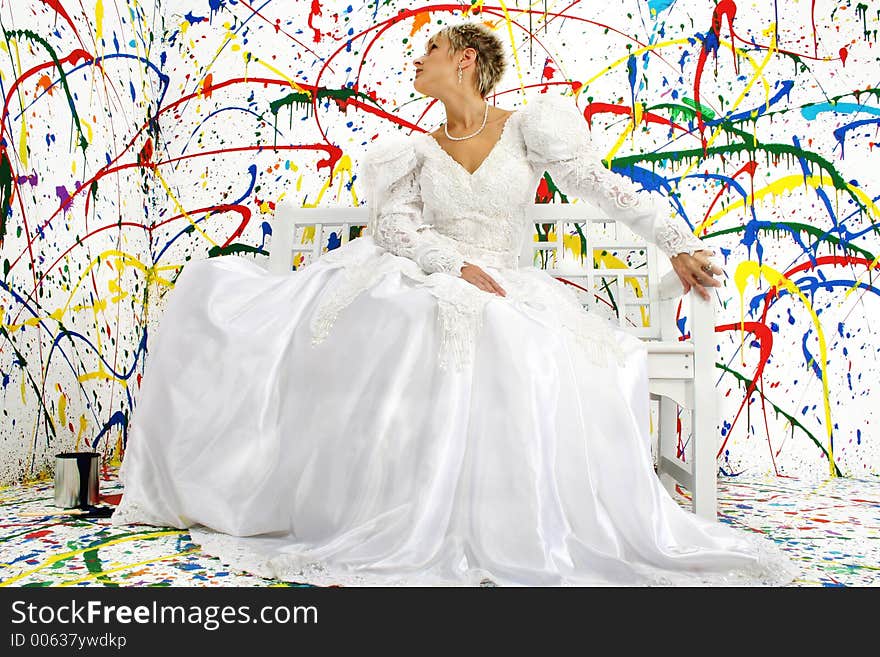 Beautiful young woman in bridal gown sitting on bench; splattered paint background. Beautiful young woman in bridal gown sitting on bench; splattered paint background