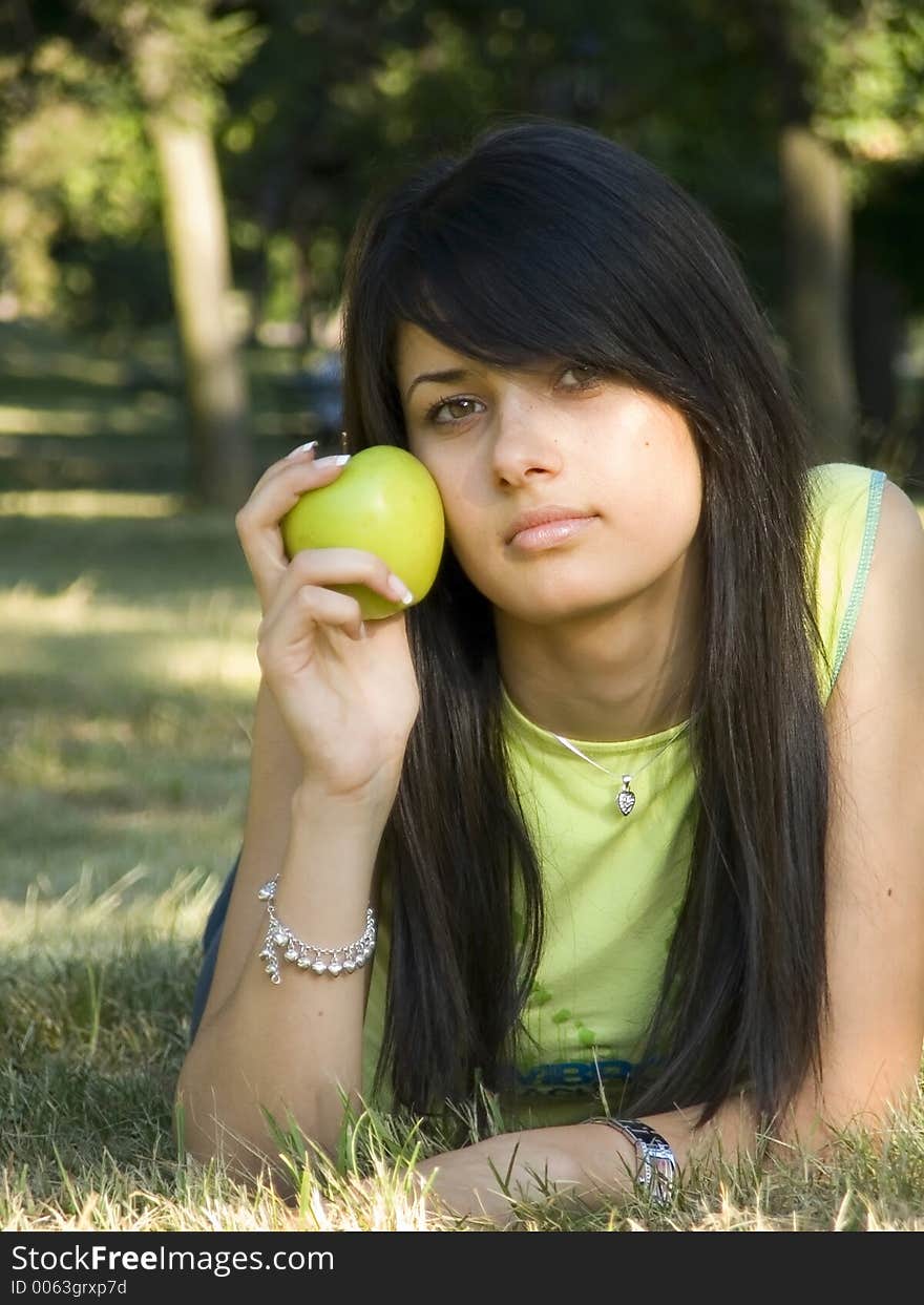 Beautiful girl lying on grass and holding green apple in hand. Beautiful girl lying on grass and holding green apple in hand