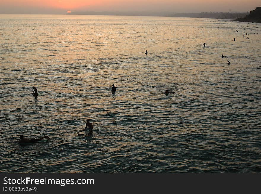 Ocean. Sunset. Many surfing guys lined up and waiting for a wave.