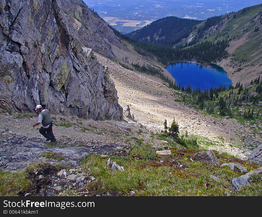 This is a picture of a hiker carefully picking his way down through the rugged and steep terrain toward the blue lake below. This is a picture of a hiker carefully picking his way down through the rugged and steep terrain toward the blue lake below.