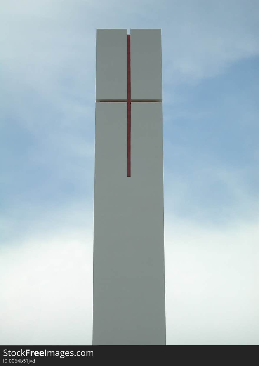 Red cross engraved in a high prismatic white stone over a cloudy sky.