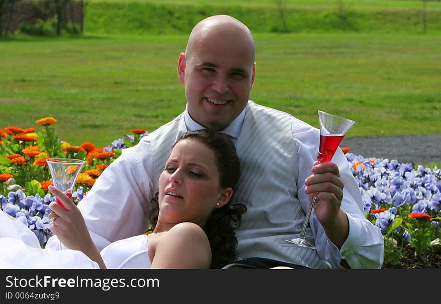 Newlywed bride and groom sitting in a bed of flowers toasting their future together. Newlywed bride and groom sitting in a bed of flowers toasting their future together