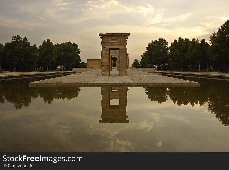 Lie-down image of a centred front perspective of the Temple of Debod in Madrid. The first arch of the monumental group is in the middle of the photo and has a line of trees at each side. The afternoon sky is the best background. A symmetry is created by the reflect of the whole enviroment in the water, that play as a mirror. Lie-down image of a centred front perspective of the Temple of Debod in Madrid. The first arch of the monumental group is in the middle of the photo and has a line of trees at each side. The afternoon sky is the best background. A symmetry is created by the reflect of the whole enviroment in the water, that play as a mirror