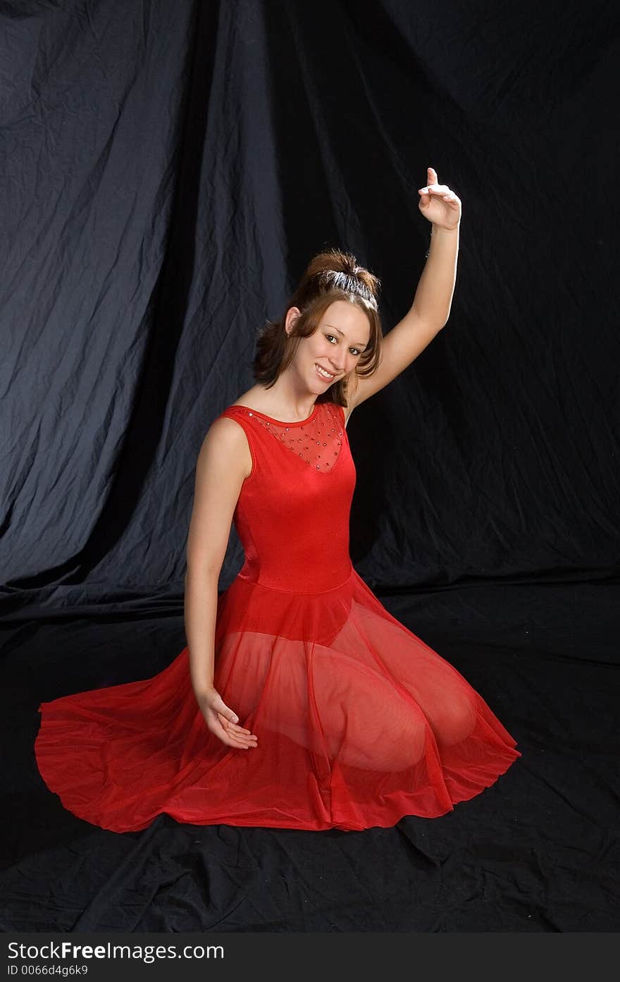 A ballerina in a red dress posed facing the camera with left arm raised.  Kneeling. A ballerina in a red dress posed facing the camera with left arm raised.  Kneeling