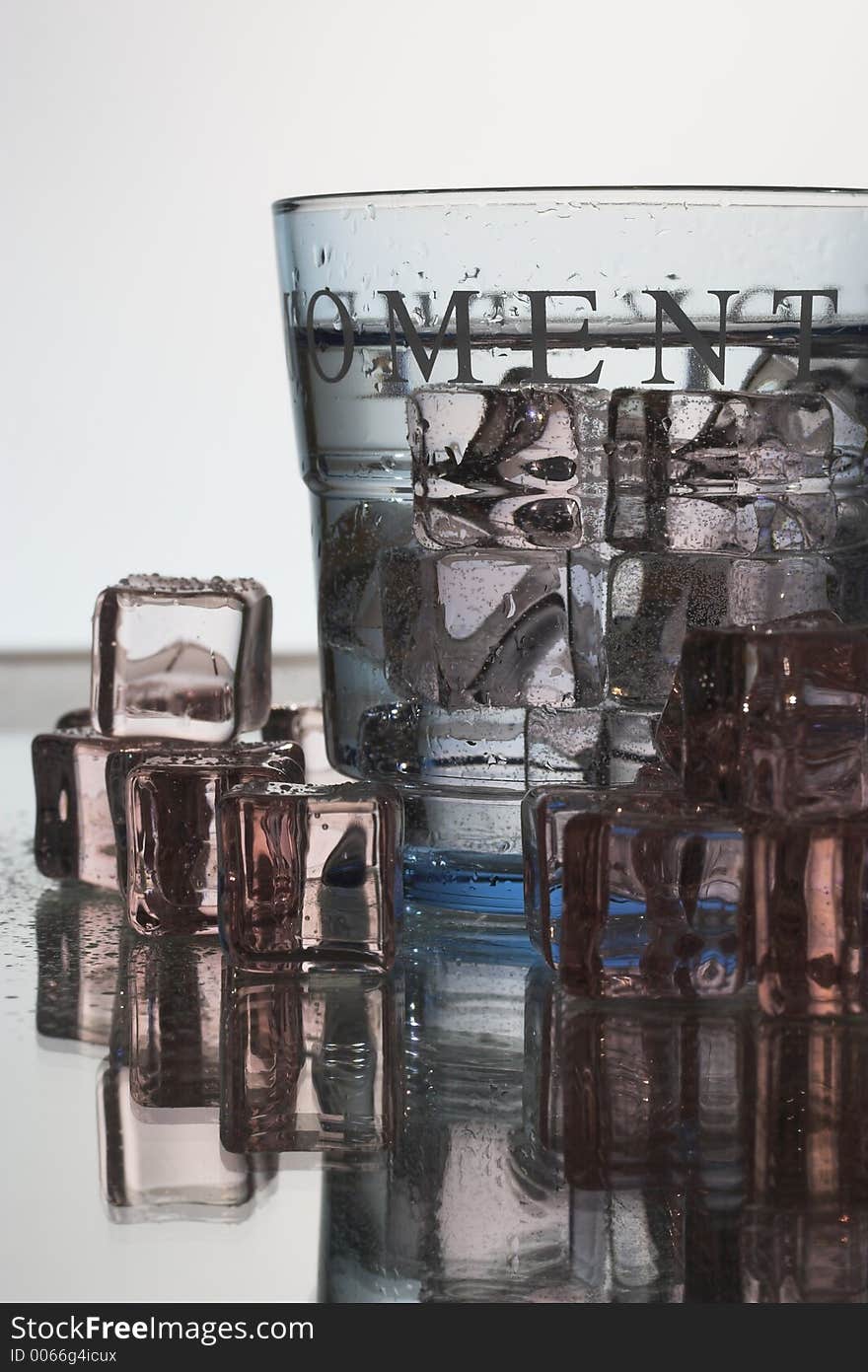 Light blue glass with ice cubes on a reflective surface