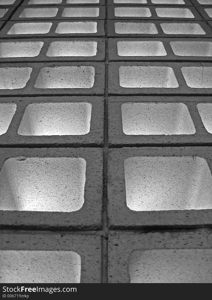 A perspective shot of a wall constructed with hollow bricks. Lights are shining through from the other side.