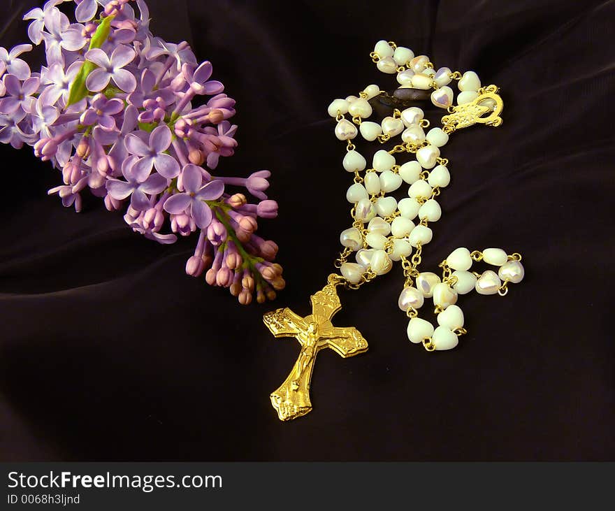 Gold Christian Catholic cross lying on elegant black veil surrounded with beautiful flower lilac, romantic gold religious jewelry with flower. Gold Christian Catholic cross lying on elegant black veil surrounded with beautiful flower lilac, romantic gold religious jewelry with flower
