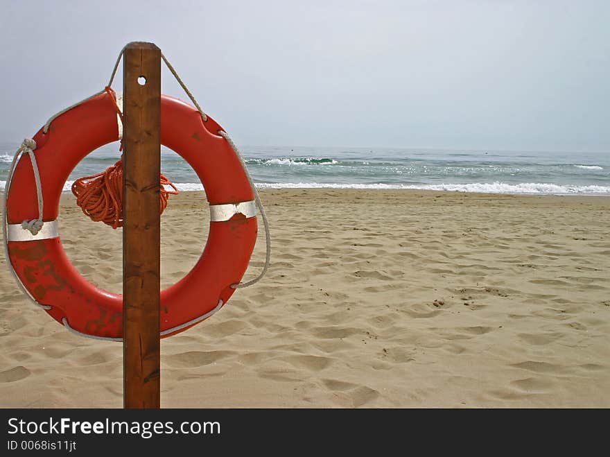 Orange life buoy hanging on a post on a sandy beach