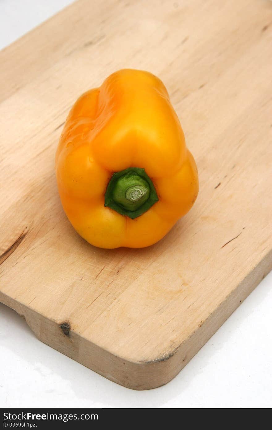 Yellow capsicum lying sideways on a wooden chopping board