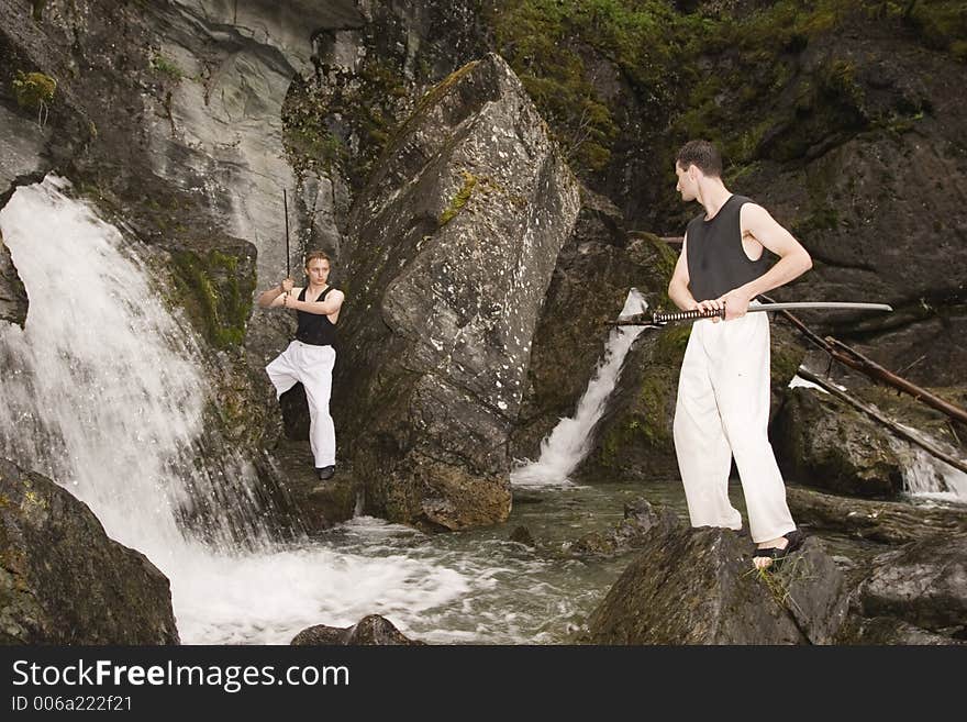 Waterfall area is a nice place to practice fencing outdoor. Two man with katanas. Waterfall area is a nice place to practice fencing outdoor. Two man with katanas