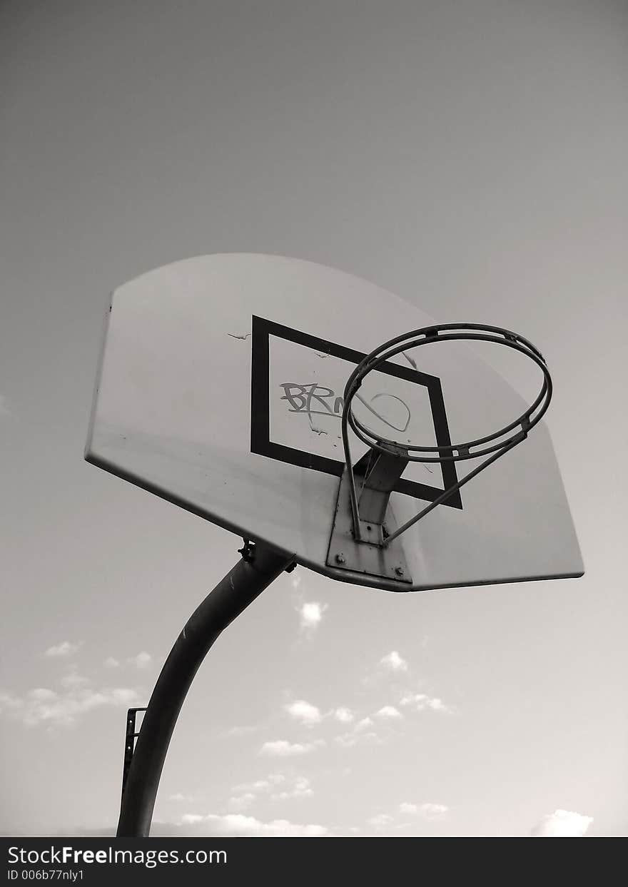 A basketball hoop without the basket netting. Graffiti was sprayed on the board. Focused at the ring.