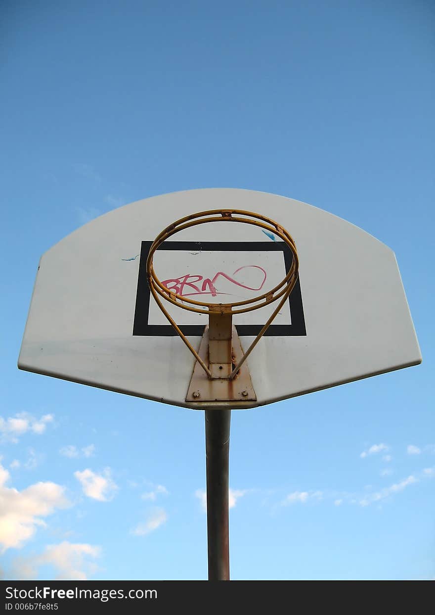 A basketball hoop without the basket netting. Graffiti was sprayed on the board. Focused at the ring.