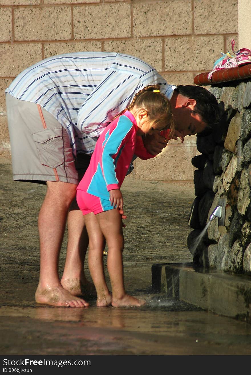 Father and daughter are washing their feet on the way home after the beach. Father and daughter are washing their feet on the way home after the beach