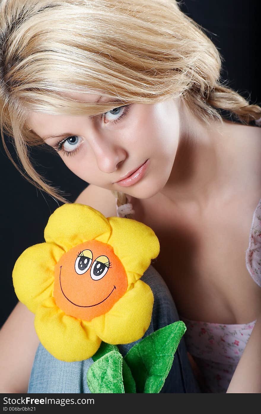 Beautiful country girl in light pink blouse and blue jeans with a flower toy, smiling. Beautiful country girl in light pink blouse and blue jeans with a flower toy, smiling