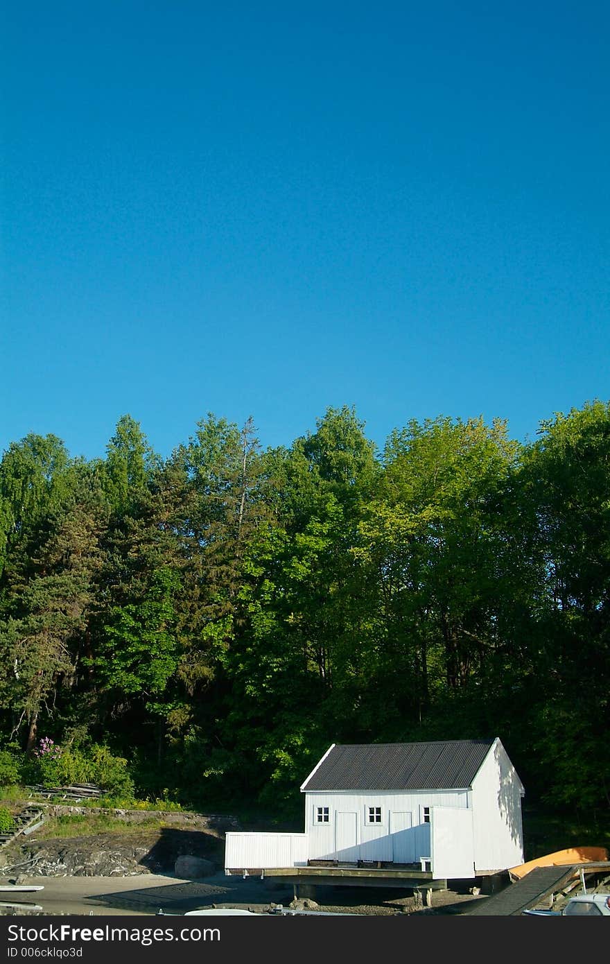 White boathouse, green forest and blue sky