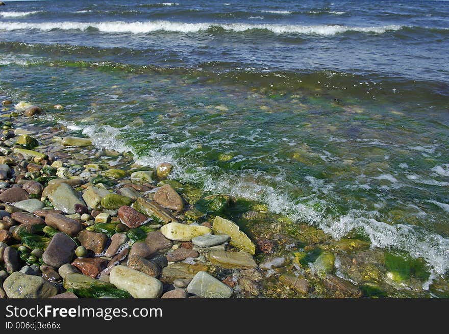 Rocks, pebbles and seaweed being washed over by little waves from sea. Rocks, pebbles and seaweed being washed over by little waves from sea